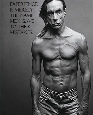 Black and white photo of Iggy pop wearing cutoff denim shorts, no shirt, scowling, scars and veins visible.